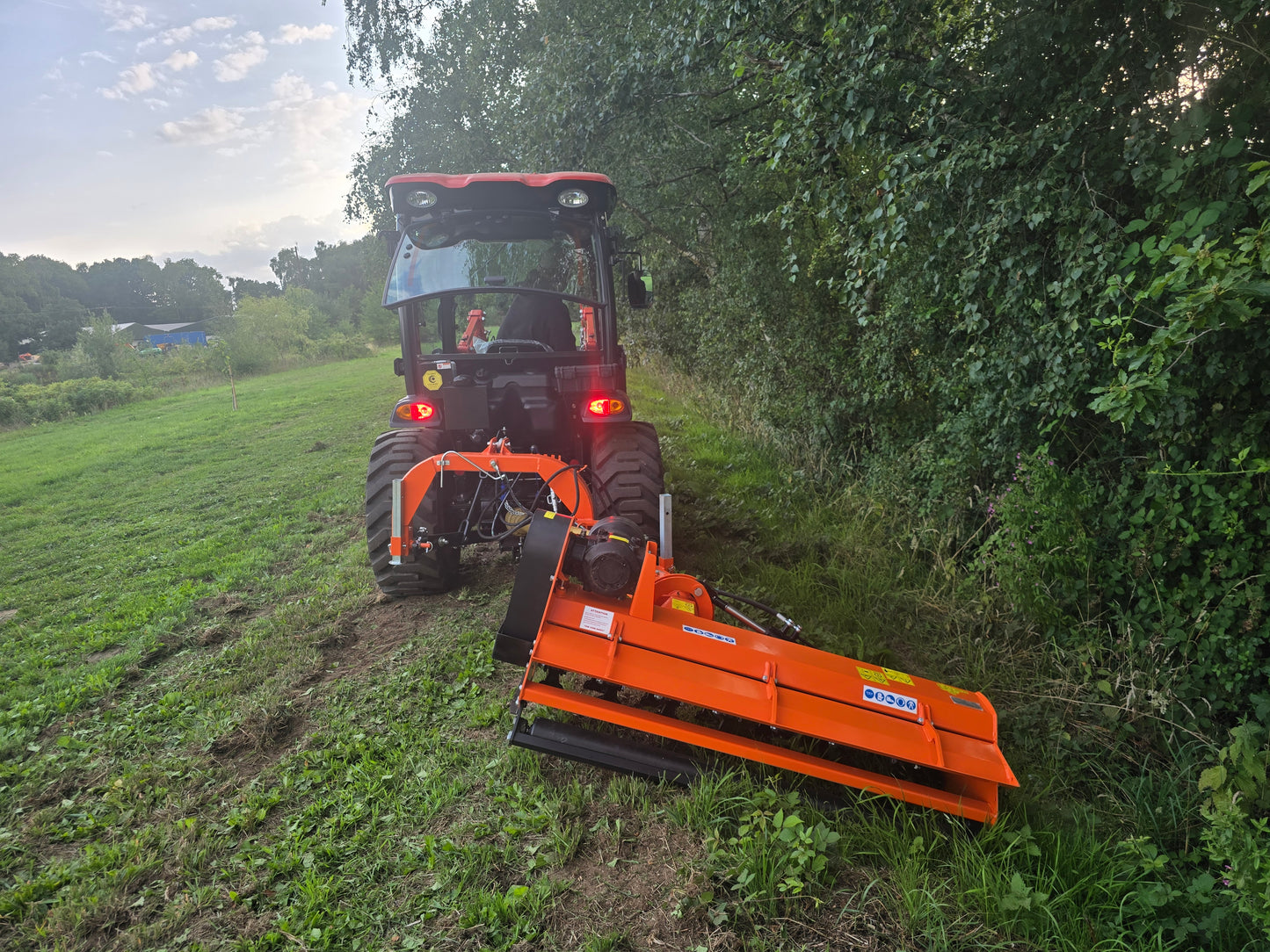 Tractor with a FarmMaster Verge Flail Mower attachment cutting through grass and brush in a field.