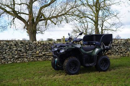 Green CFMOTO ATV parked near a stone wall with trees in the background