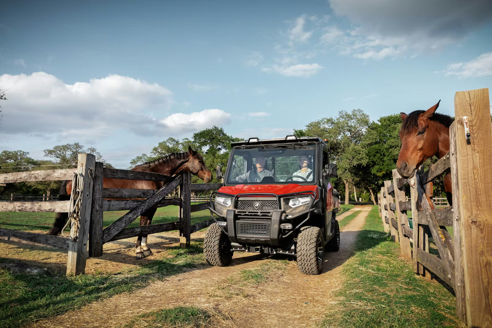Two people in a Kioti K9 utility vehicle on a dirt path with horses on either side.
