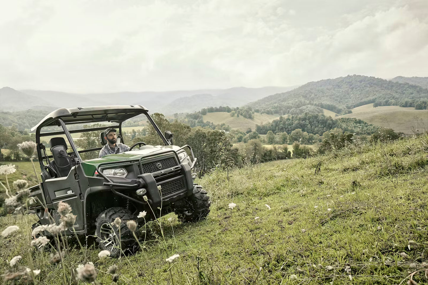 Kioti K9 utility vehicle on a grassy hillside with mountains in the background