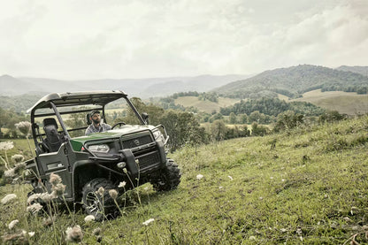 Kioti K9 utility vehicle on a grassy hillside with mountains in the background