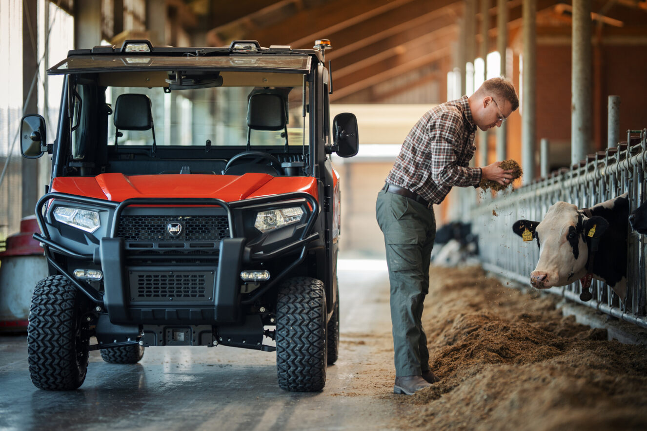 Man interacting with a cow in a barn next to a Kioti utility vehicle
