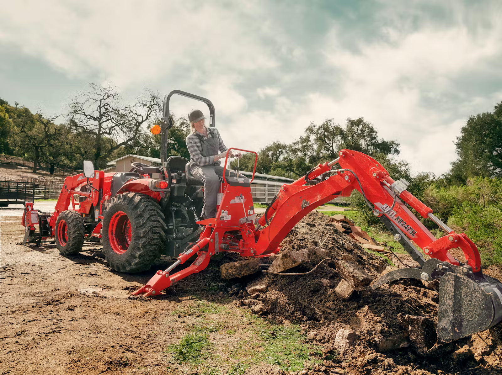 Red Kioti excavator being operated on a construction site with trees in the background