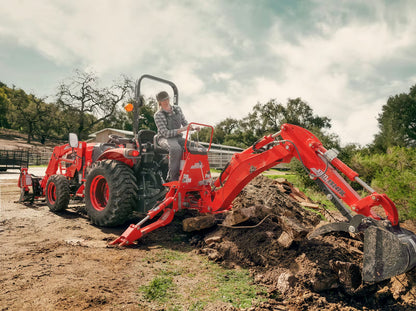 Red Kioti excavator being operated on a construction site with trees in the background