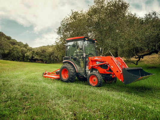 Orange Kioti tractor with a front loader in a grassy field with trees in the background