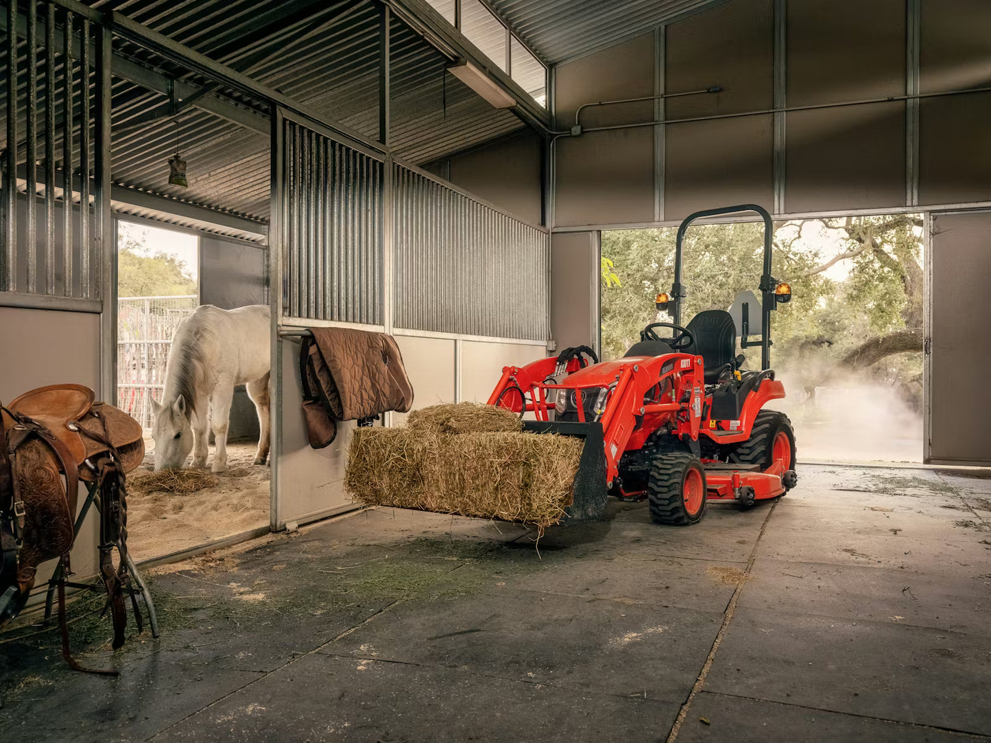 Kioti compact tractor loading hay into a barn with a horse in the background