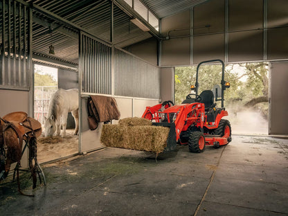 Kioti compact tractor loading hay into a barn with a horse in the background