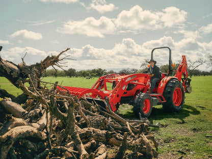 Red Kioti tractor with a backhoe attachment in a field with trees and a person sitting on it.