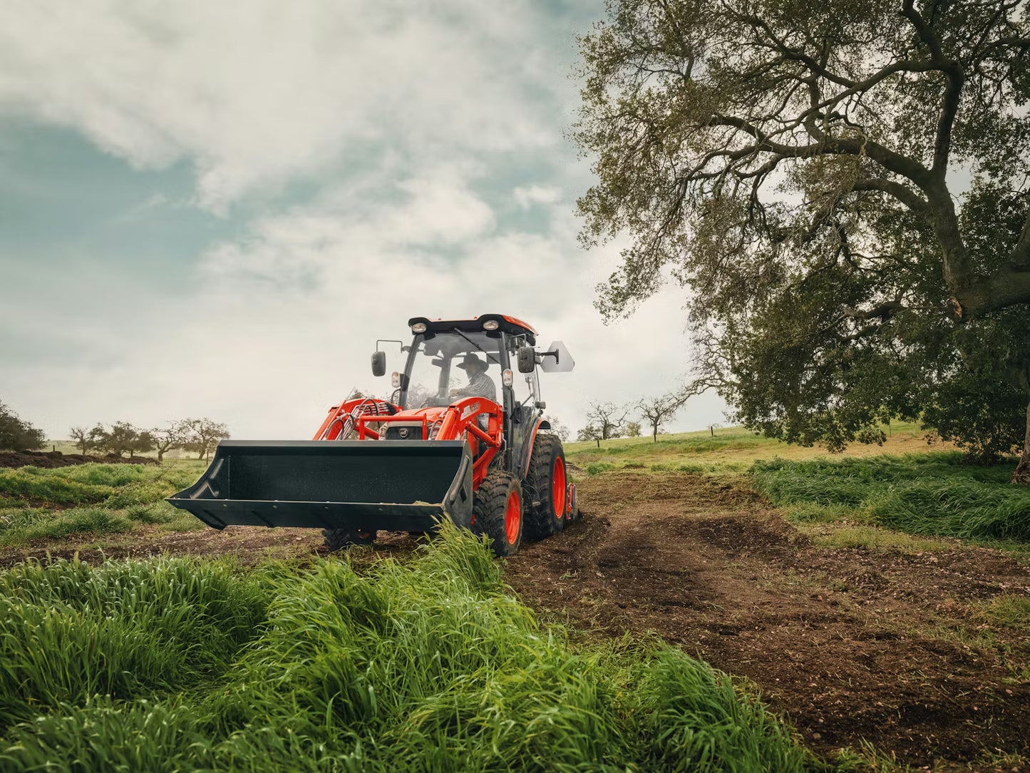Kioti Tractor working in a field with trees and sky in the background