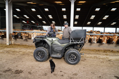 Two people standing next to a CFMOTO quad bike in a barn with cows in the background