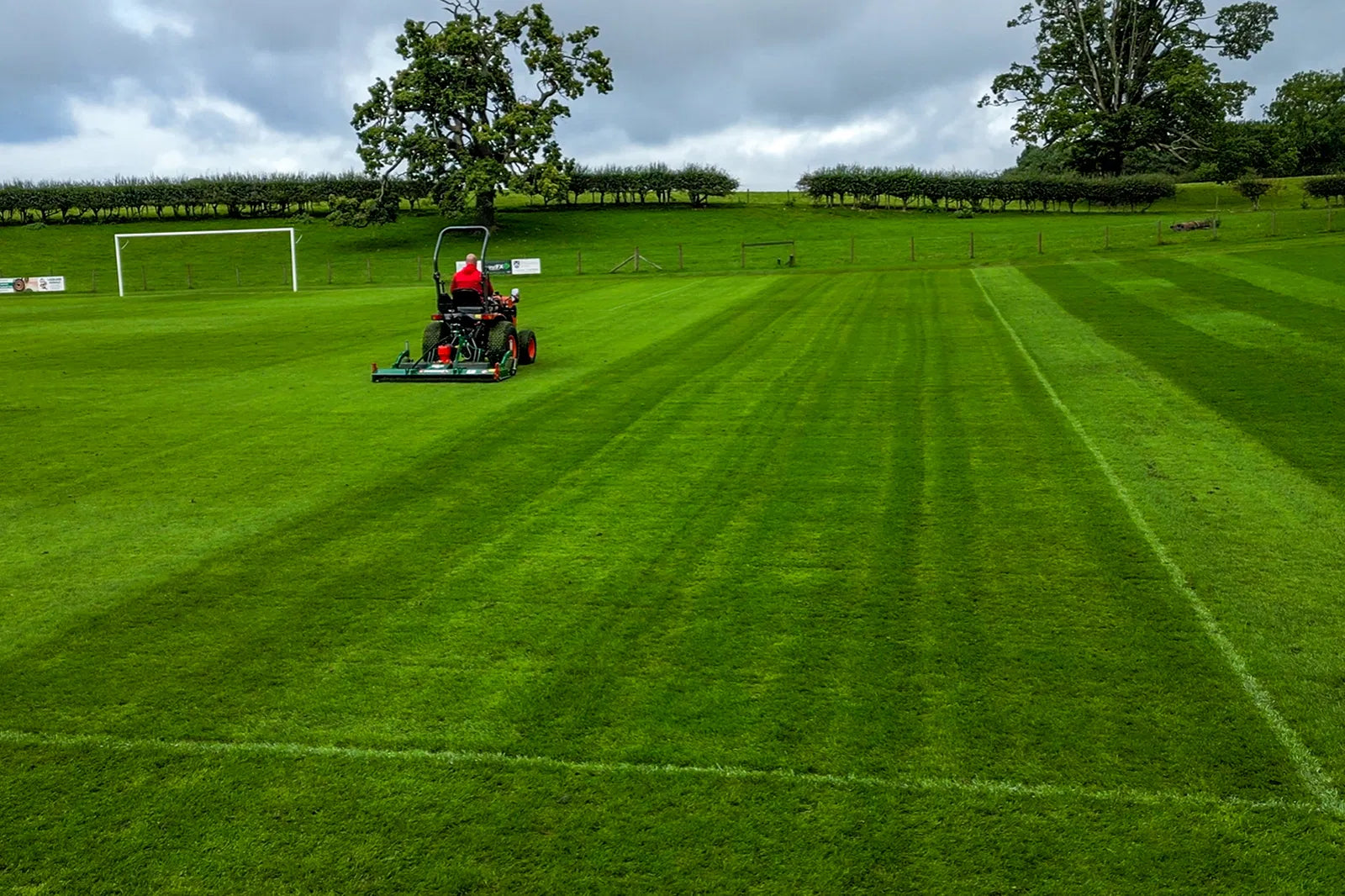 Wessex finishing mower on a well-maintained grass field with trees and a cloudy sky in the background.