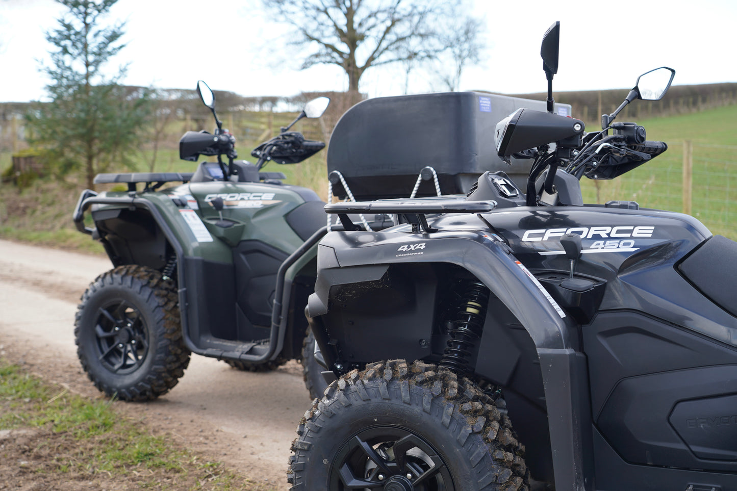 CFMOTO 450 and 520 ATVs on a dirt road with a grassy field in the background.
