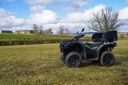 Green CFMOTO ATV parked on a grassy field with a rural landscape in the background