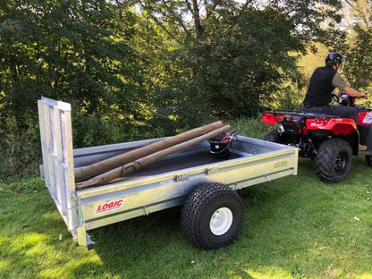 Logic ATV Trailer with logs on a grassy area next to an ATV.
