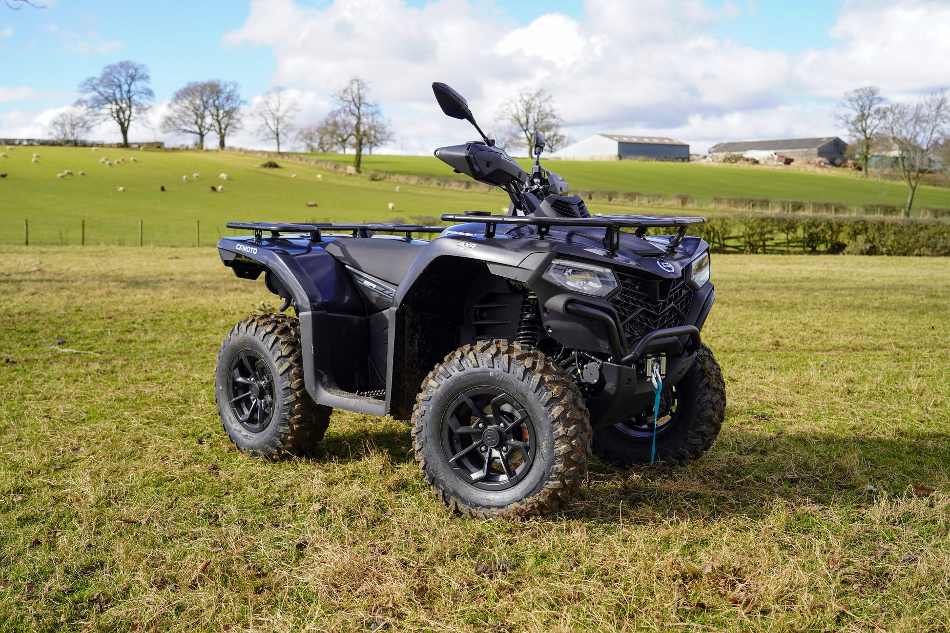 Black CFMOTO quad bike parked on a grassy field with a rural landscape in the background