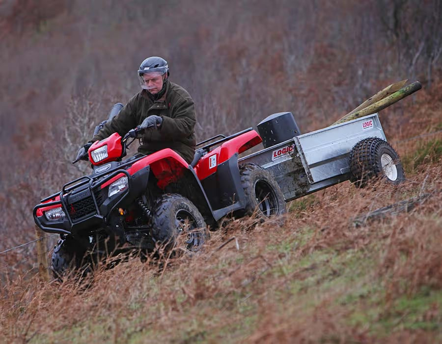 Person riding a red ATV with a trailer attached through a forested area.
