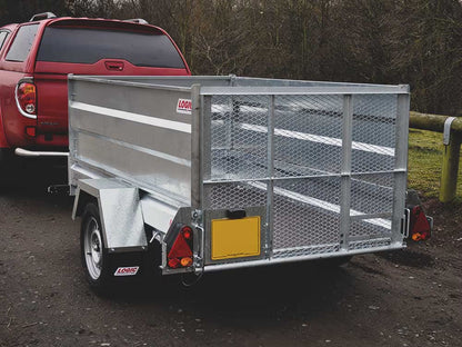 Metal trailer attached to a red pickup truck on a dirt road with trees in the background.