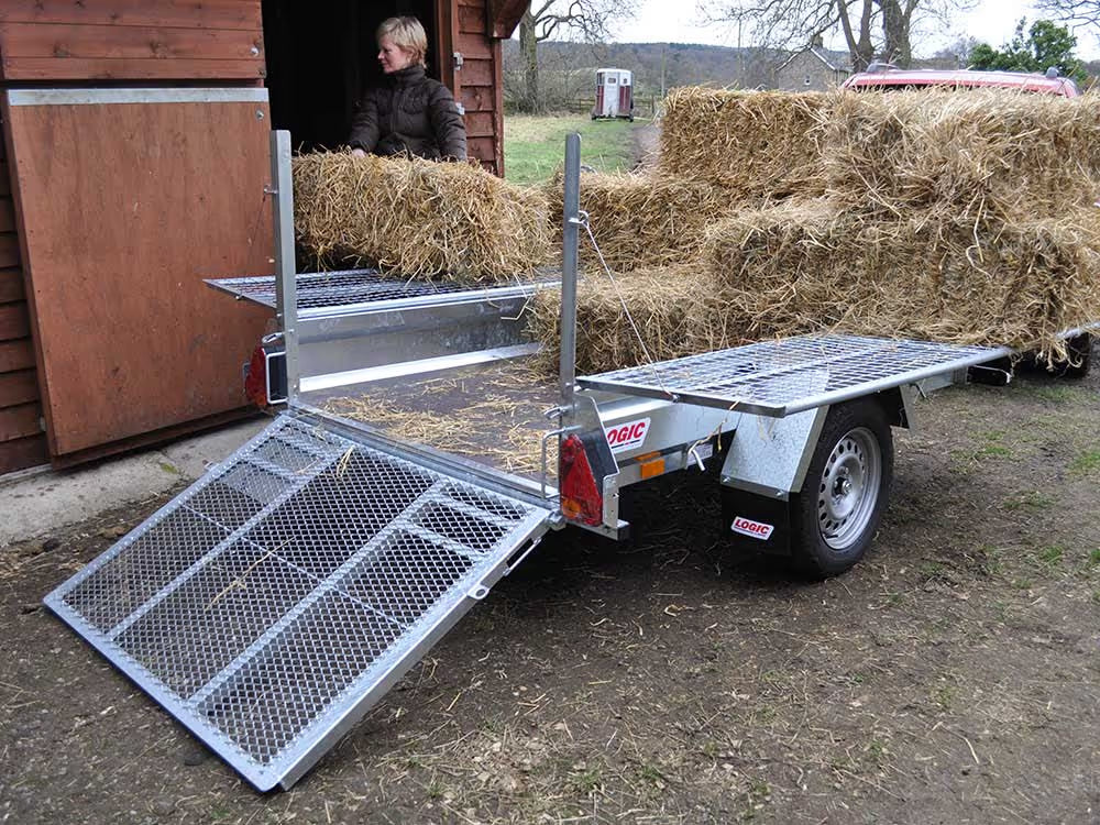 Trailer loaded with hay bales next to a wooden building