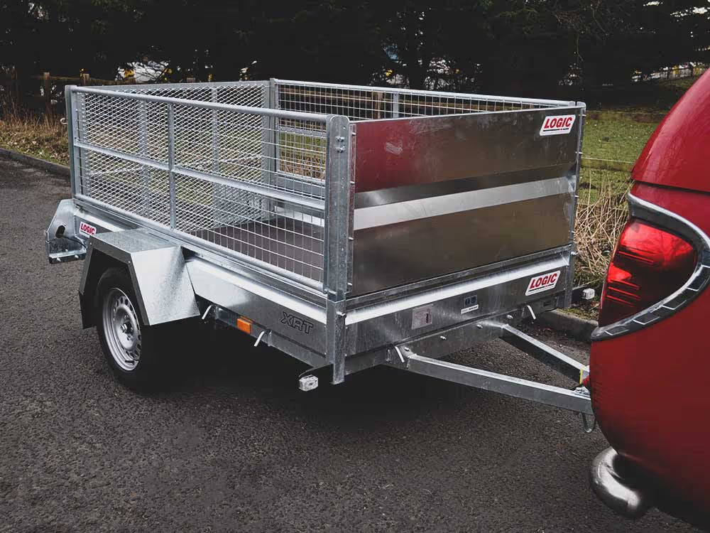 Metal trailer with a cage attached to a red vehicle on a road.