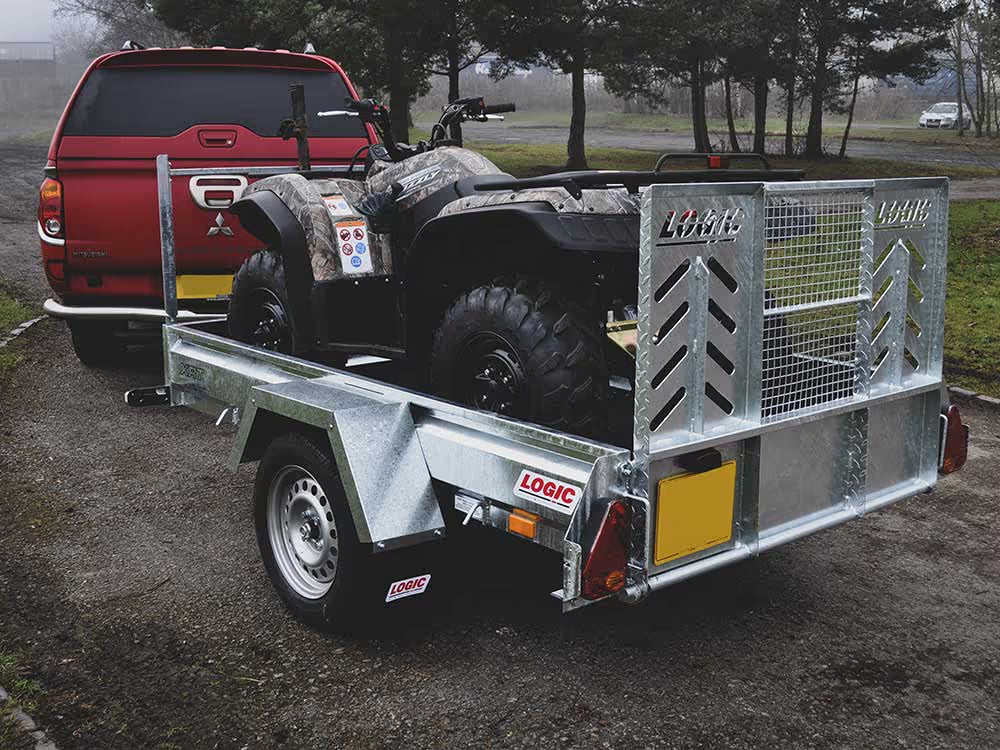 Red truck towing a trailer with an ATV on a gravel road.
