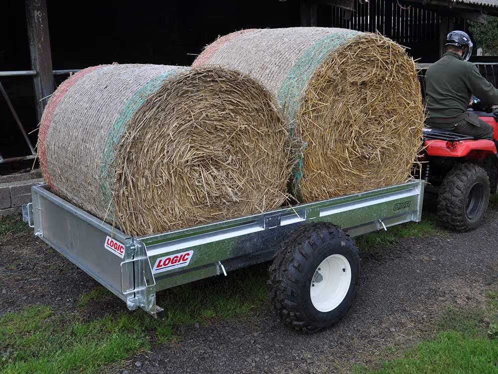 Hay bales on a trailer with a person on an ATV in the background