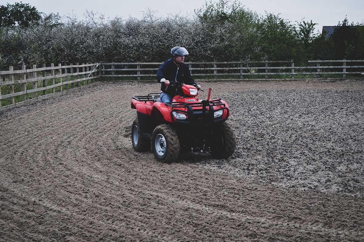 Person riding a red ATV on a muddy field with a chain harrow