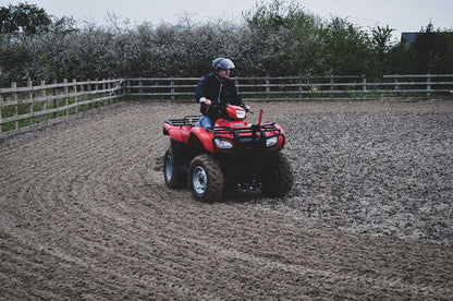 Person riding a red ATV on a muddy field with a chain harrow