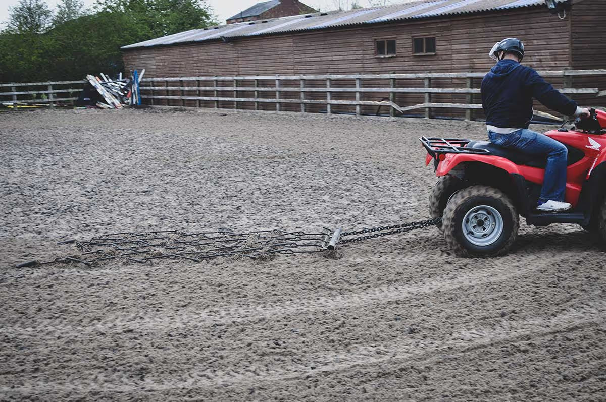 Person riding a red ATV in an outdoor setting with a chain harrow