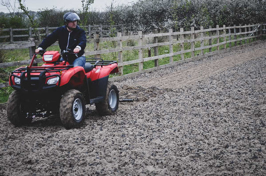 Person riding a red ATV with a chain harrow