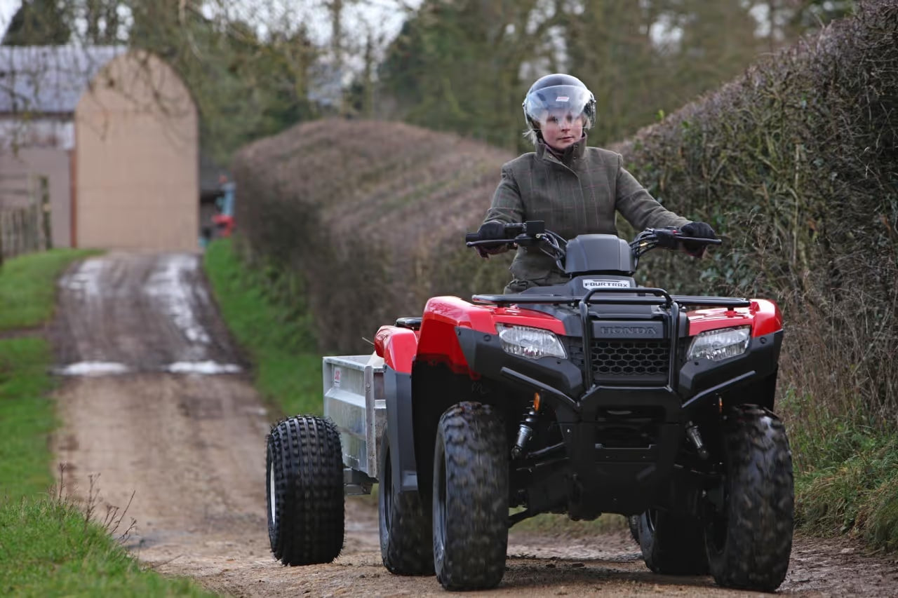 Person riding a red ATV on a dirt path with a Logic ATV Trailer