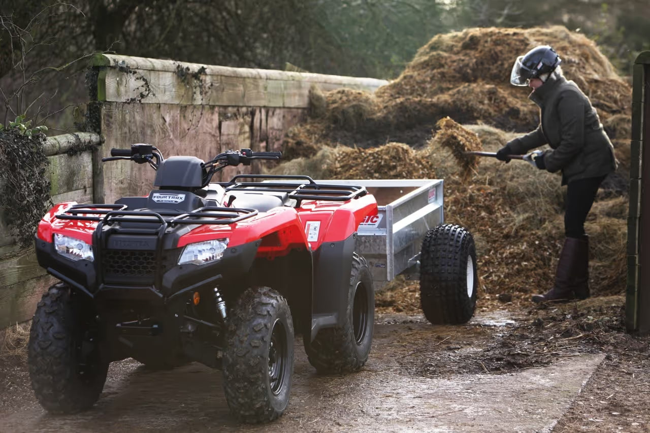 Red and black ATV with a trailer attached, being used to move hay.
