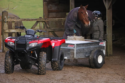 Red ATV towing a trailer with a horse and person in a stable setting