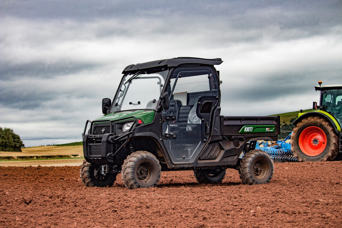 Utility vehicle towing a tractor on a plowed field with a cloudy sky.