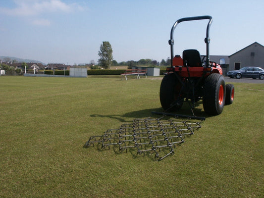 Tractor with a chain harrow attachment on a grassy field