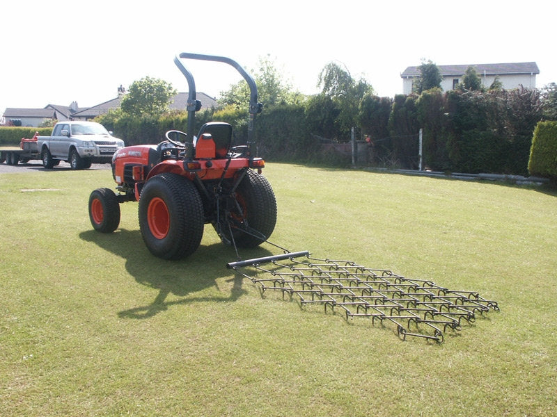 Red tractor with a chain harrow attachment on a grassy field