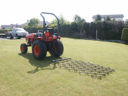 Red tractor with a chain harrow attachment on a grassy field