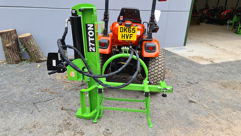 Green FarmMaster Goliath tractor log splitter attached to an orange Kioti tractor in a workshop setting.