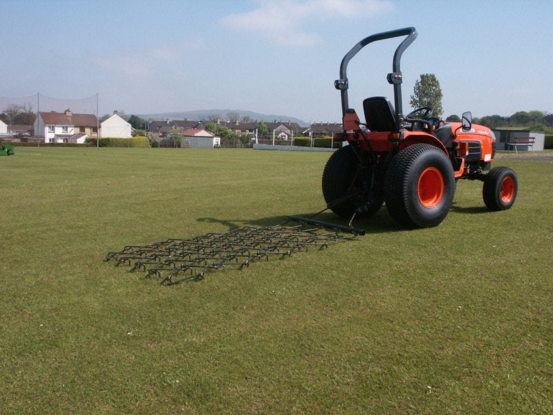 Red tractor with a chain harrow attachment on a grassy field
