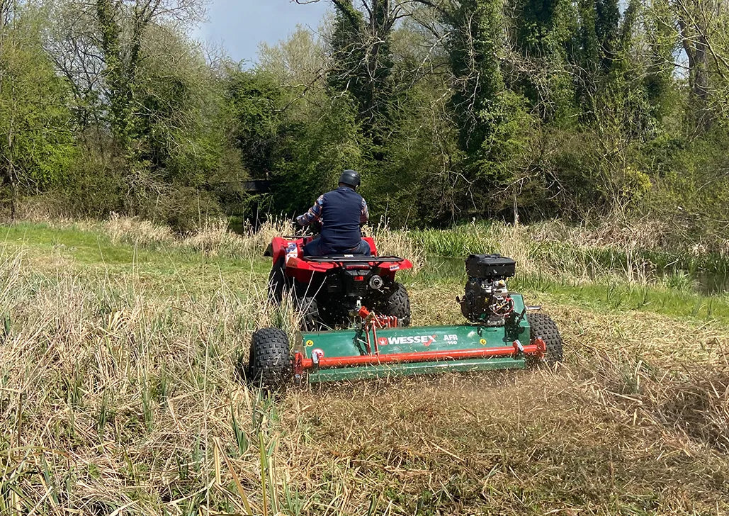 Person operating a red ATV with a Wessex ATV flail mower attachment in a grassy field.