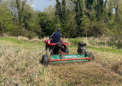 Person operating a red ATV with a Wessex ATV flail mower attachment in a grassy field.