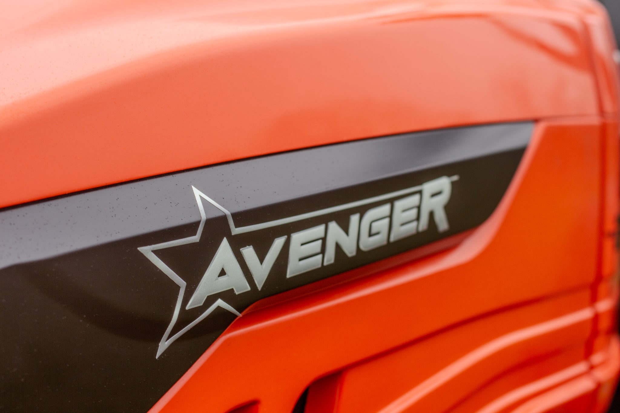 Close-up of an orange compact tractor with 'Avenger' branding on a black background