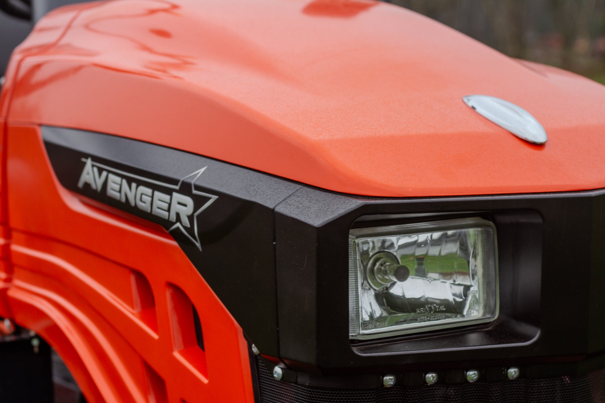 Close-up of an orange Avenger vehicle with a headlight and logo.