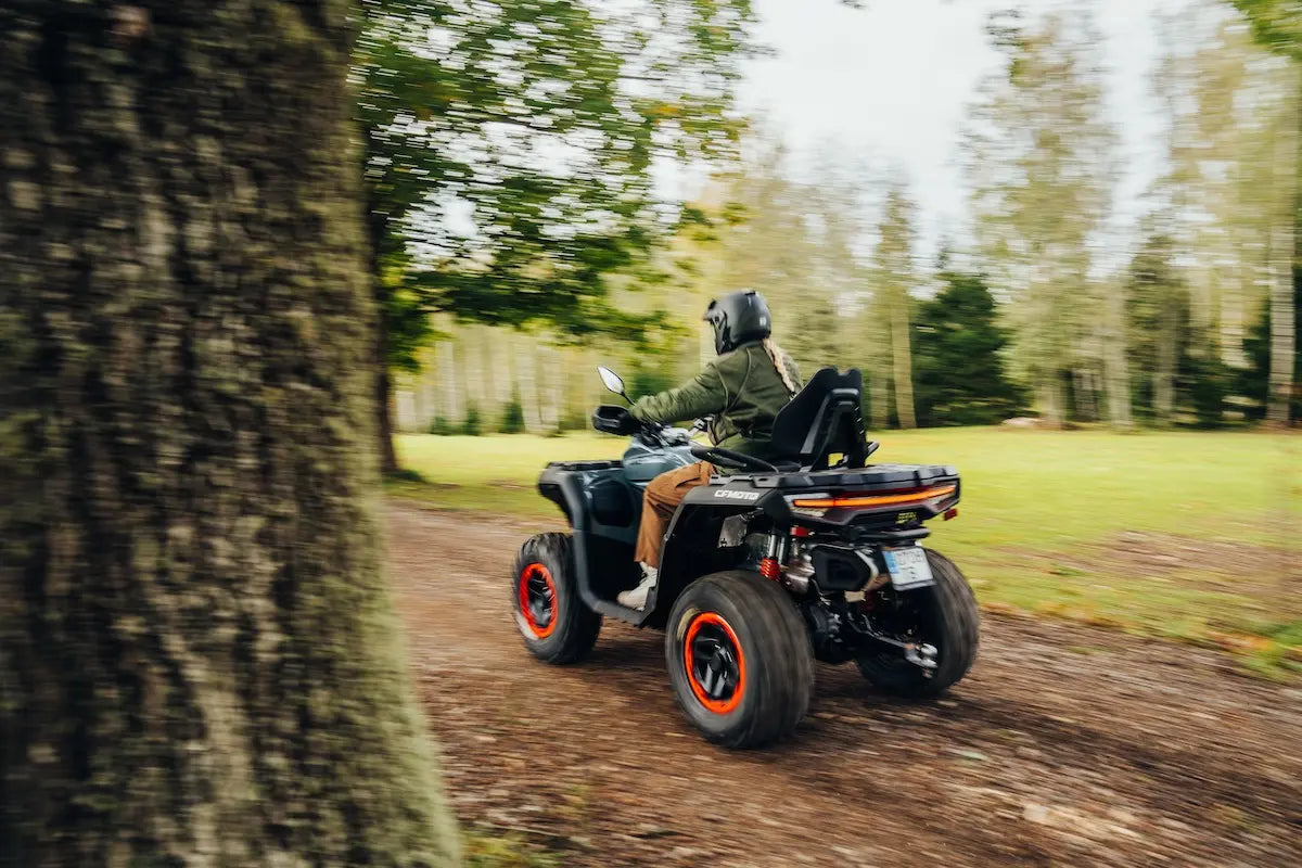 Person riding a CFMOTO ATV through a forested area