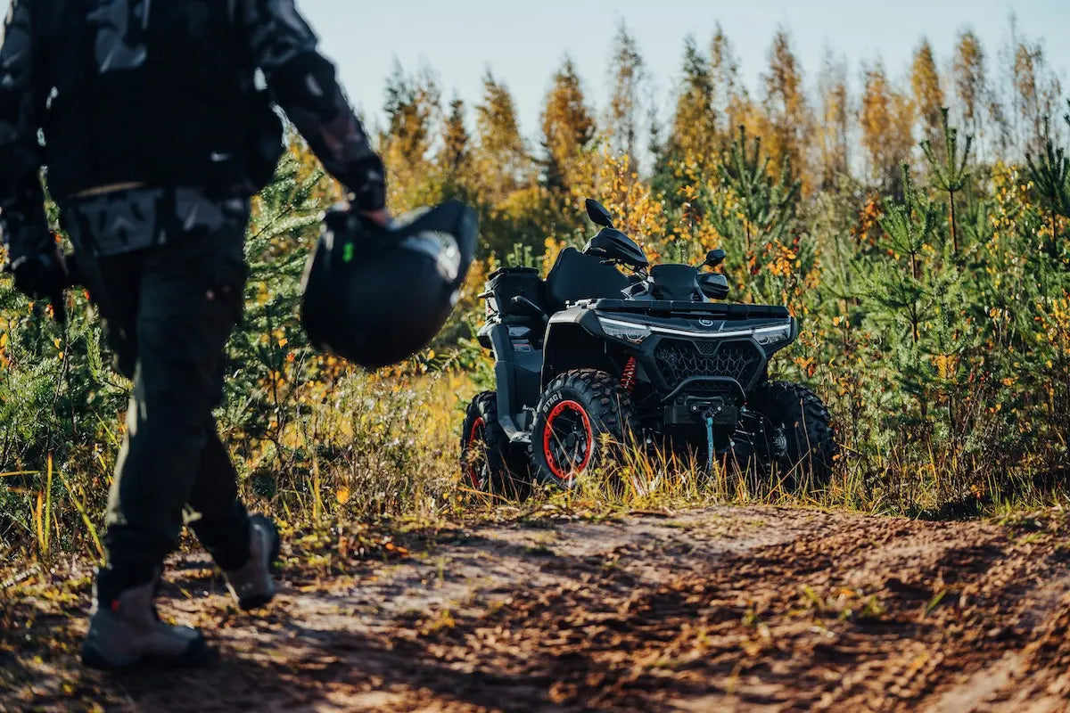 Person walking with a helmet towards a CFMOTO quad bike on a forest trail