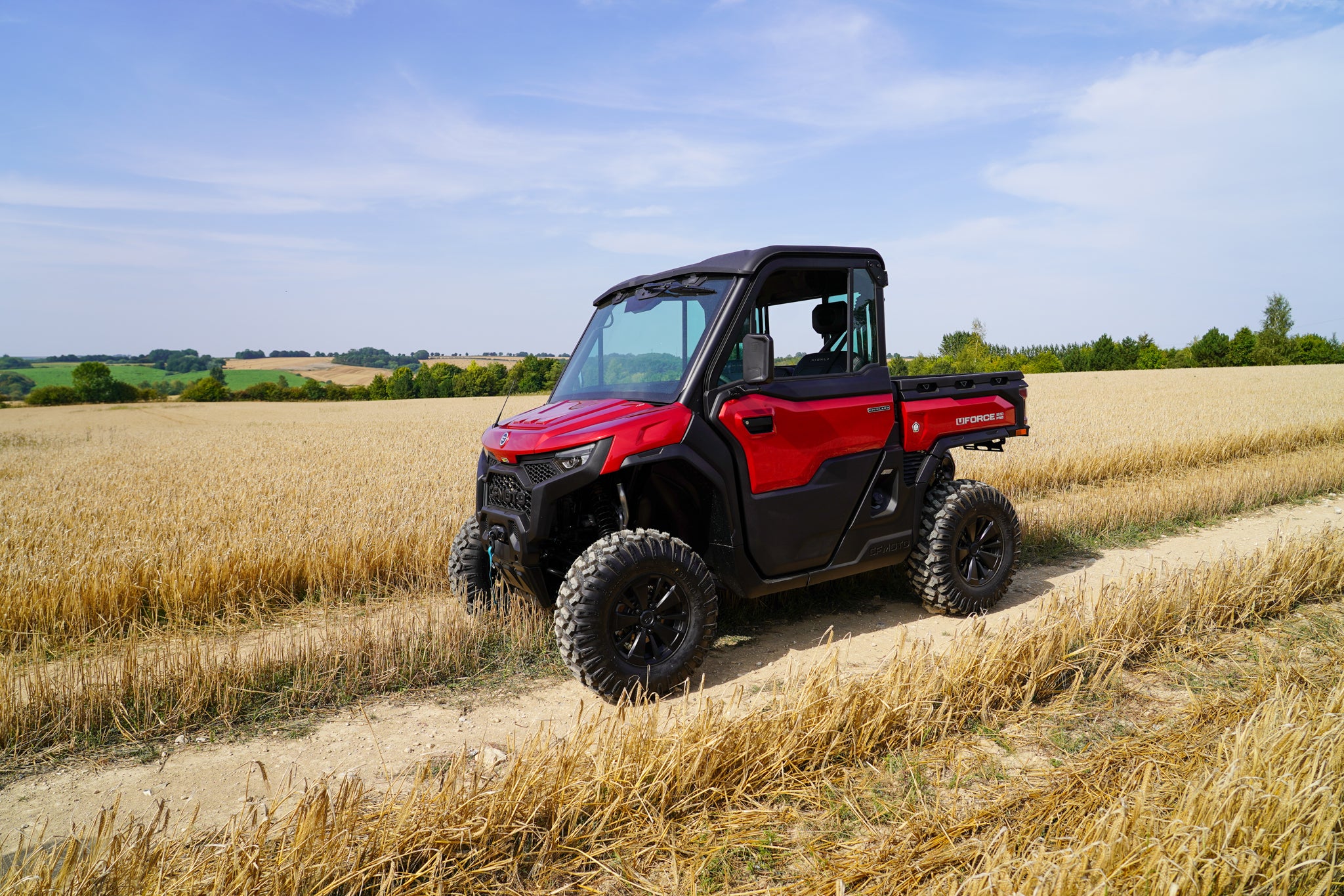 Red and black CFMOTO U10 Pro UTV on a dirt path in a field with a blue sky.