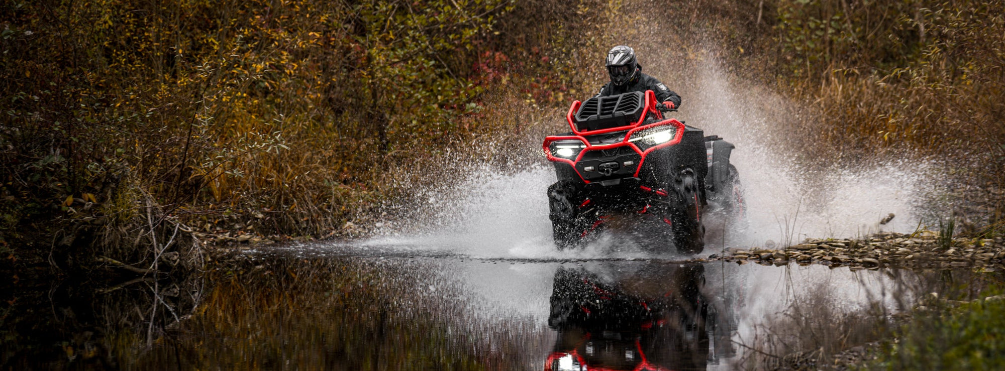 Person riding a CFMOTO 1000 MV ATV through water in a forest setting
