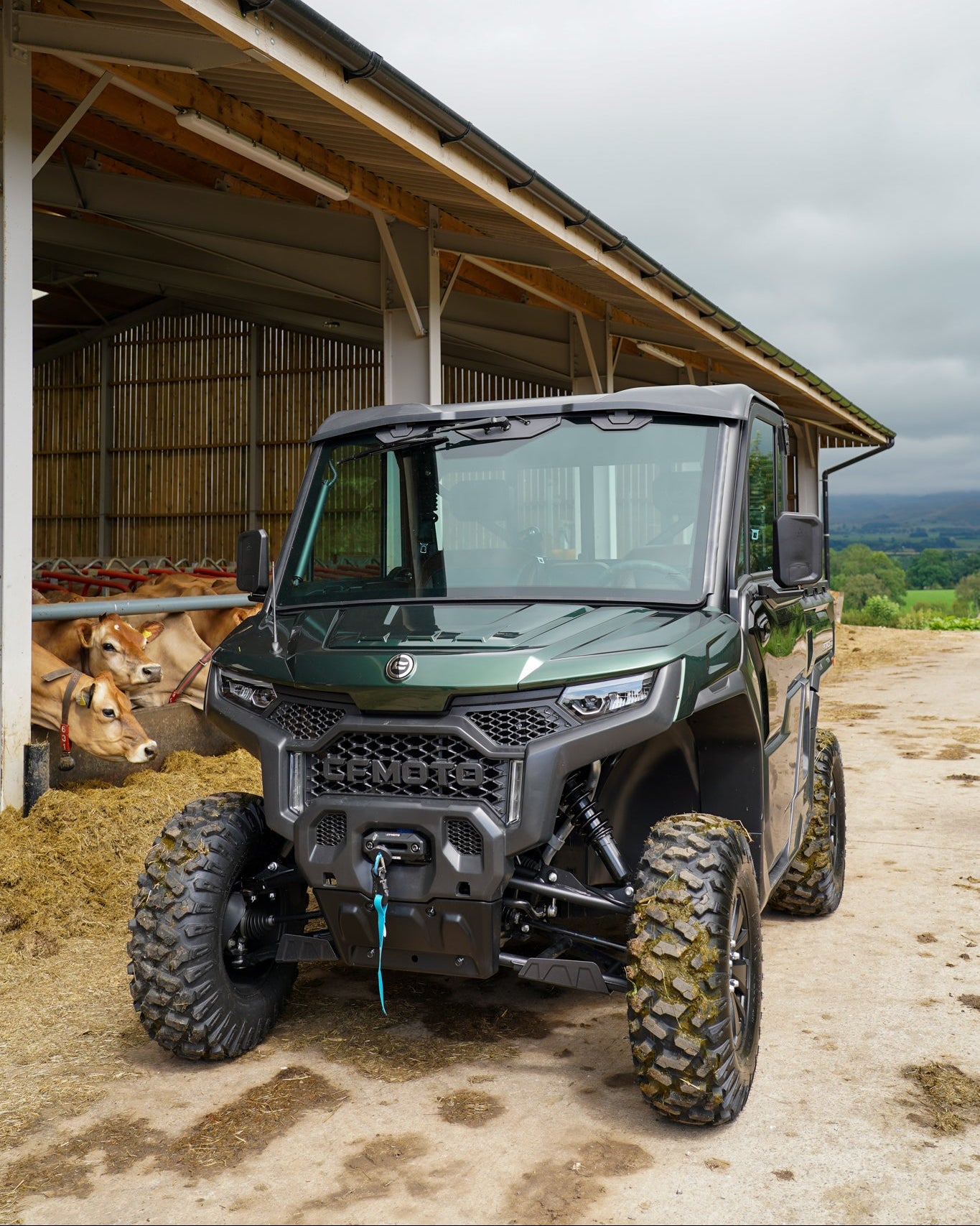 Green CFMOTO U10 Pro utility vehicle parked in front of a barn with cows inside