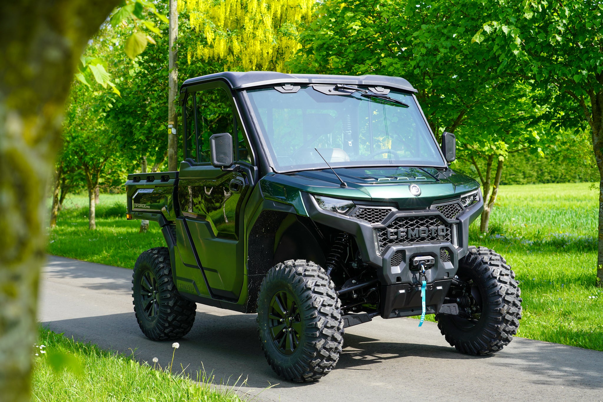 Green CFMOTO U10 Pro off-road vehicle on a paved path with trees in the background