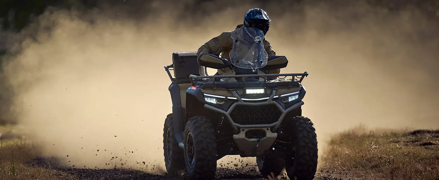 Person riding a CFMOTO quad bike through a dusty landscape