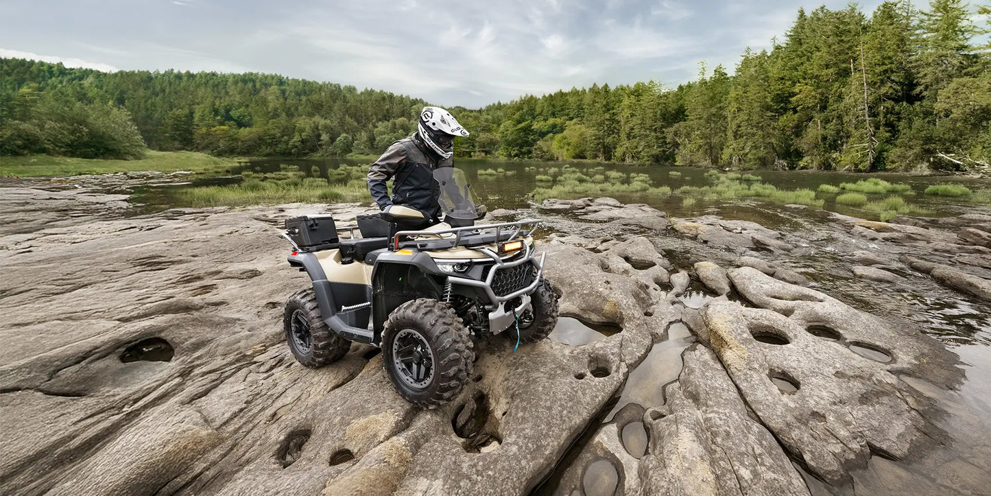Person riding a CFMOTO quad bike on rocky terrain with a forest in the background